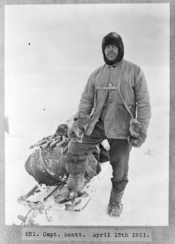 Sir Robert Falcon Scott standing next to his sledge in expedition clothing.