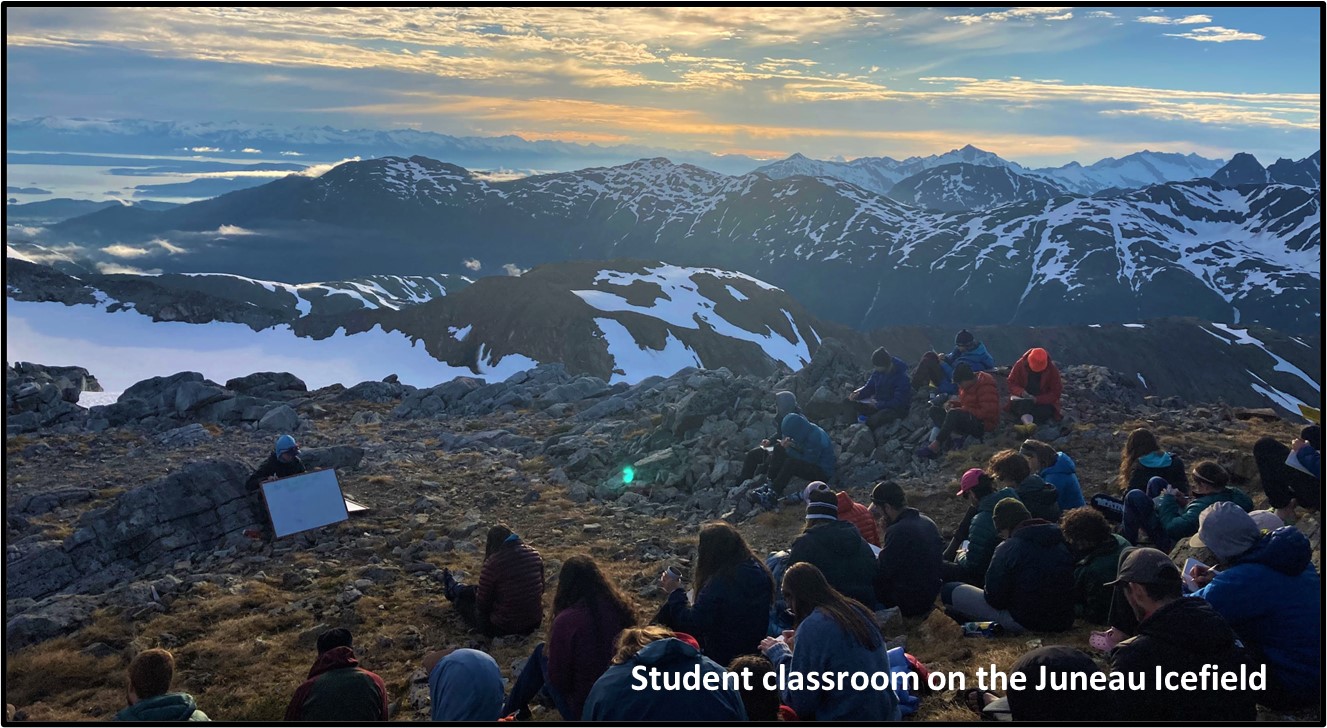 A group of students learning about the physics of glaciers while sitting on a bedrock outcrop on the edge of the Juneau Icefield. Summer 2021. Photo by Scott Braddock