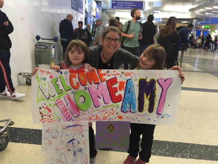 A woman and two little girls with a Welcome Home sign