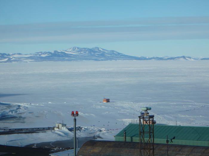 View of sea ice, mountains, and orange dive huts.