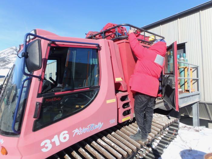Loading bags on top of a pisten bully, a big red track vehicle.