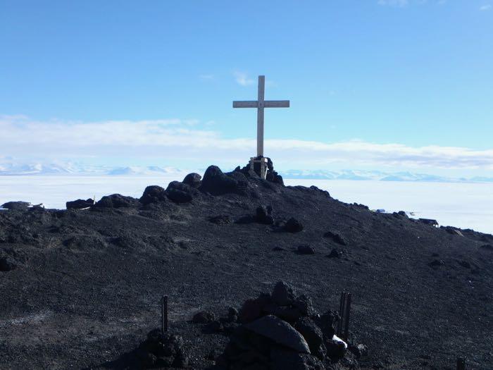cross on a hill with sea ice and mountains in the background