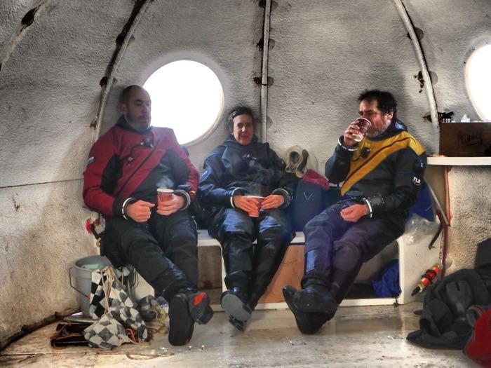 Three divers in dry suits drinking hot chocolate