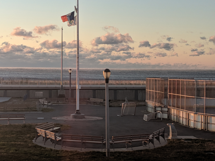 Image shows a boardwalk, a hockey rink, and an ocean view in the background. 