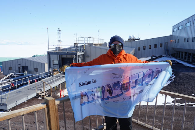 Tara holds up a flag that reads Elaine in Antarctica. 
