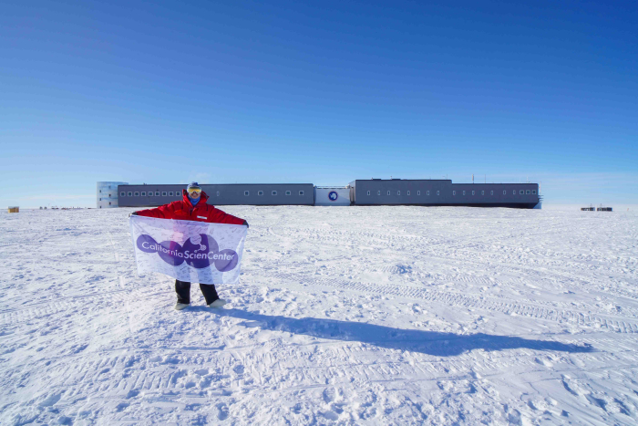 Elaine stands in front of the South Pole Station with the California Science Center Flag