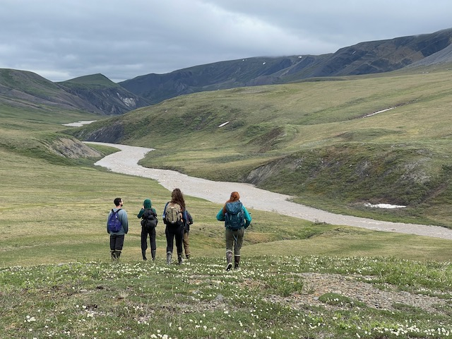 A group of hikers walk in a field alongside a meandering river. 