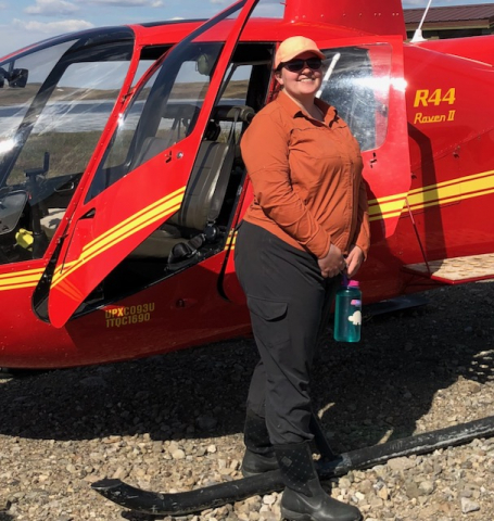 Liza Backman stands in front of a red helicopter ready to head out for field work. Photo taken by Lexy Salinas. 