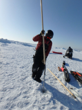 Inserting tilt meter into two inch hole in sea ice. 