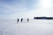 Three people waving in front of the South Pole Station