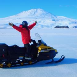 Person with arms raised on a snow machine on the sea ice. A volcanic mountain is in the background.